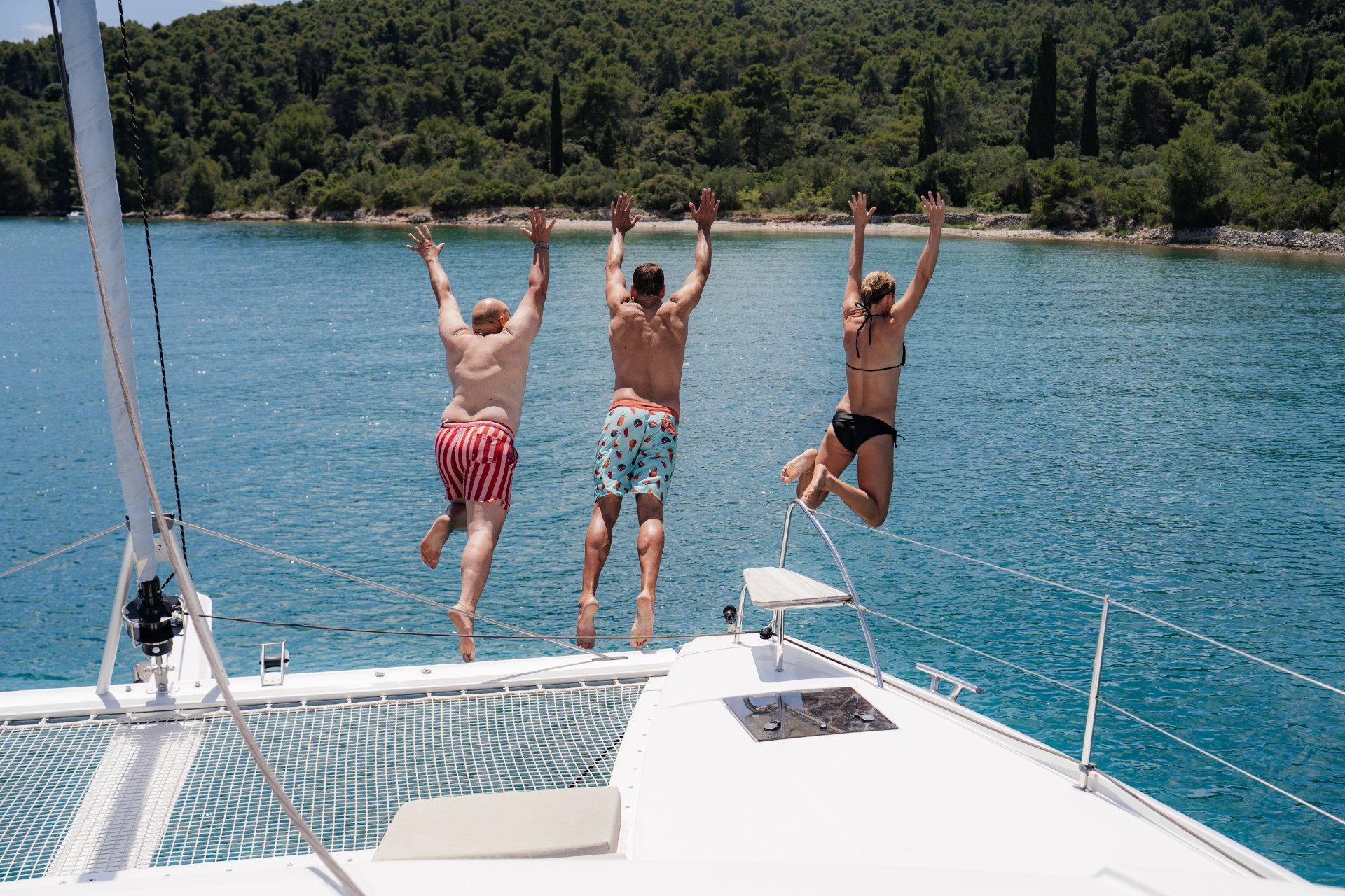 Personen springen von einem Katamaran ins blaue Wasser einer kroatischen Bucht.